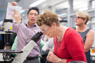 Dr Jason Tye-Din talks to the Coeliac Victoria and Tasmania group while a woman looks down a microscope