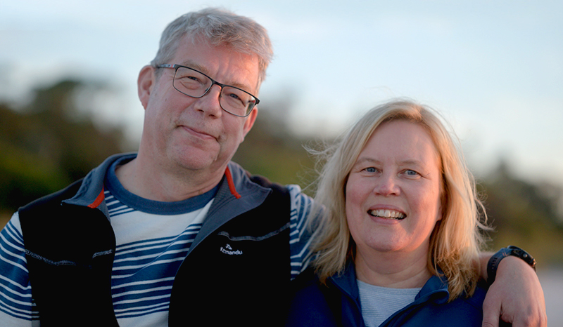 Raimo wearing a striped top and polo fleece vest has his arm around his wife Tiina.